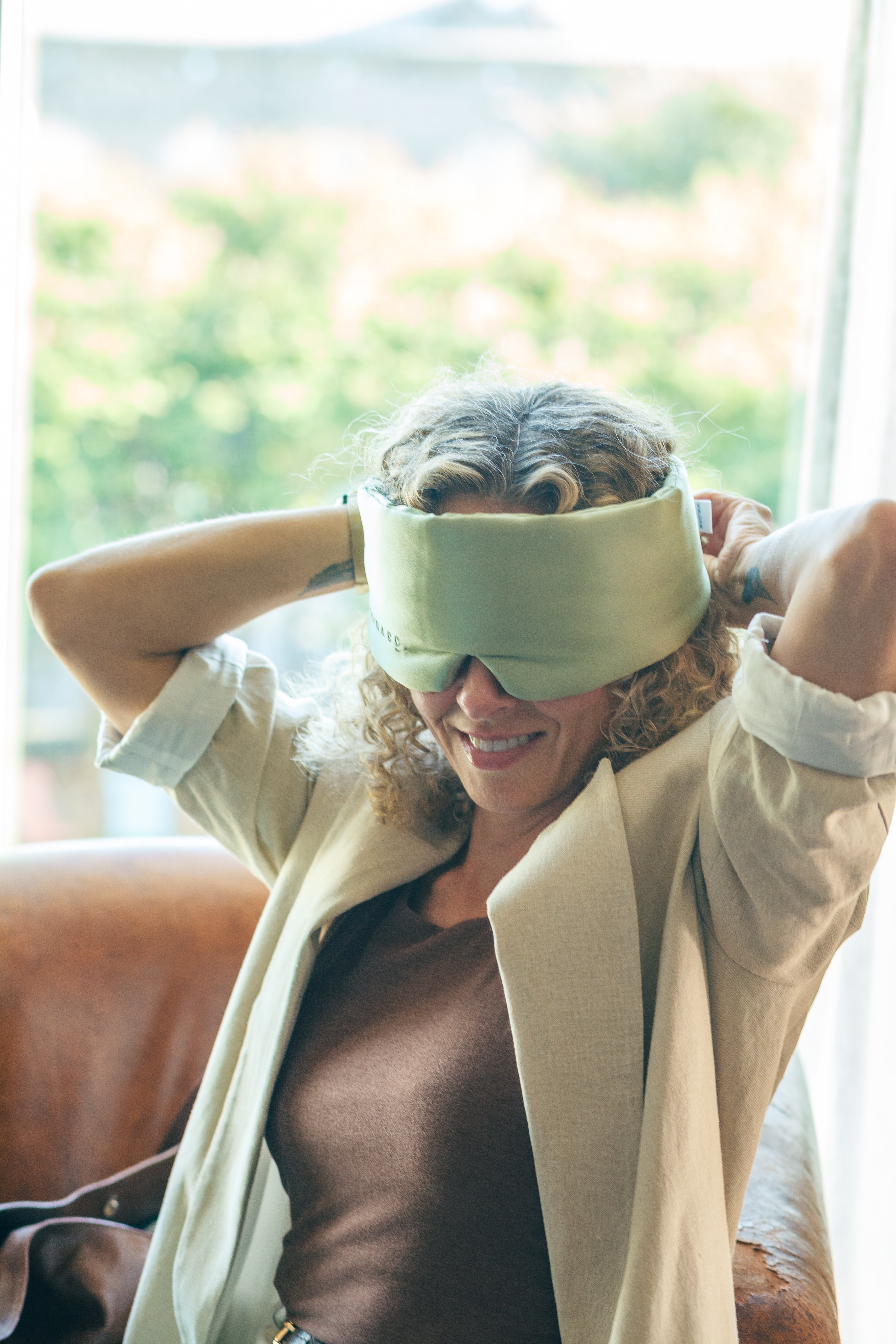 Woman wearing a green sleep mask indoors with a blurred background