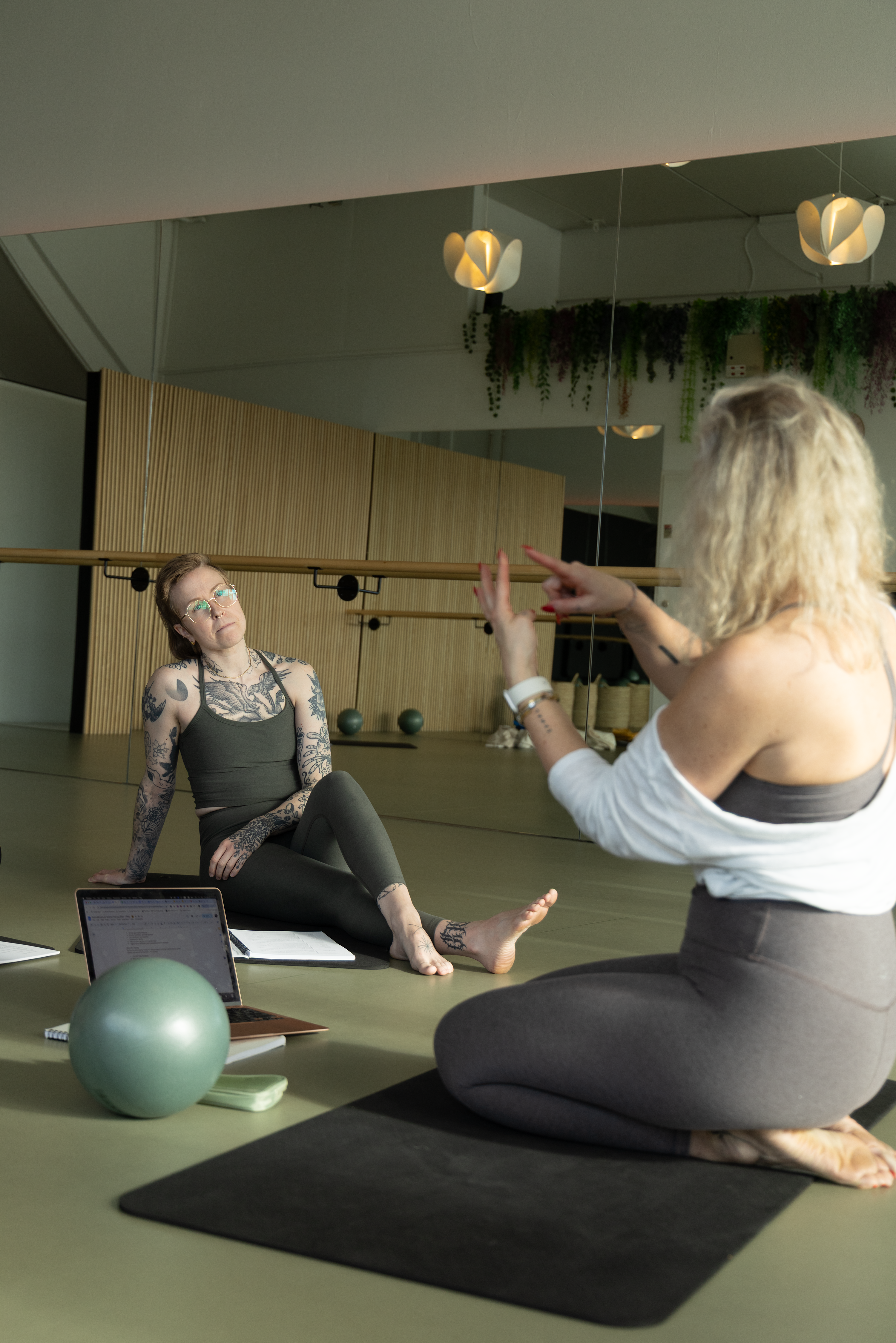 Two women practicing yoga in a studio with mirrors and exercise balls.