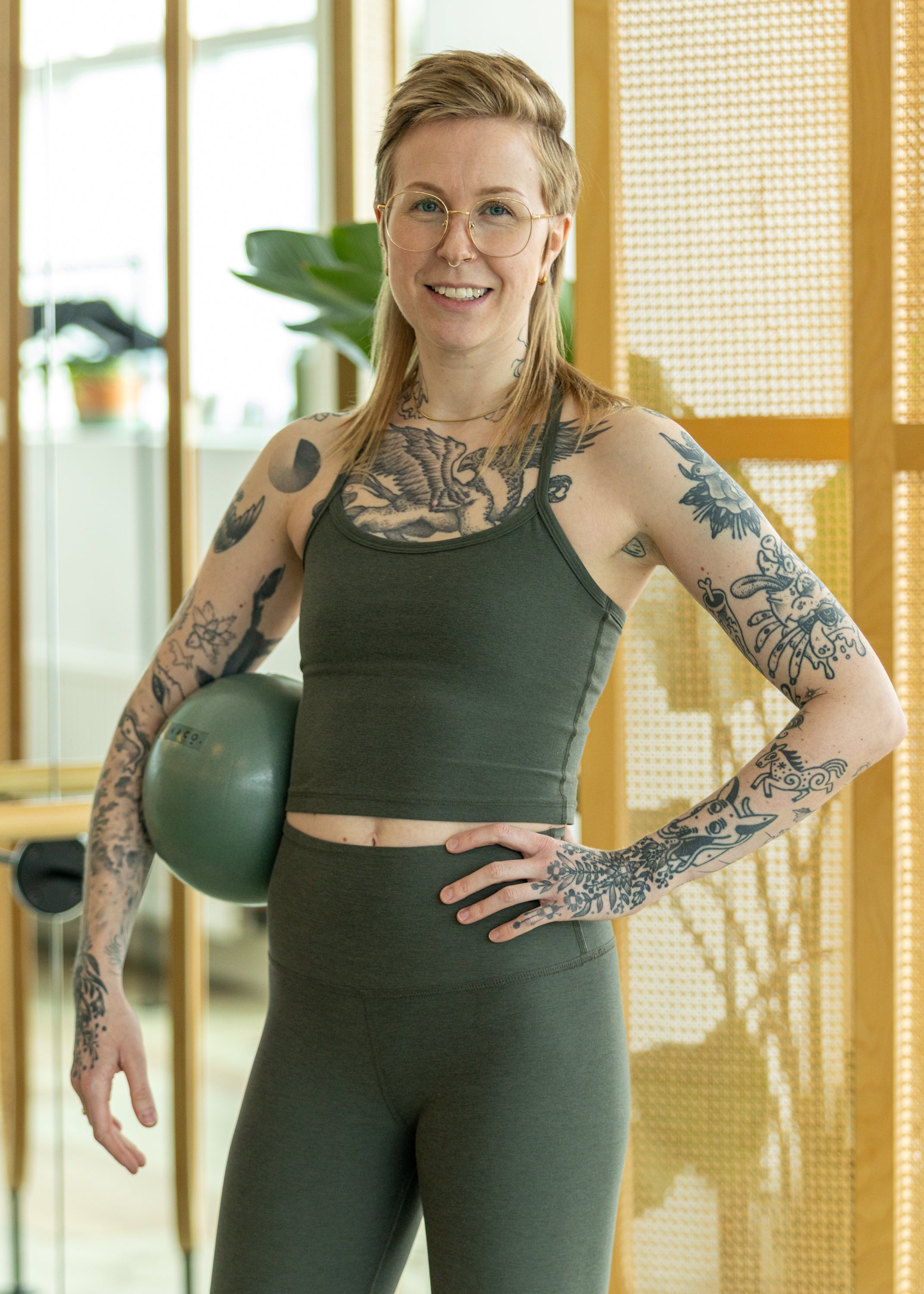 Person wearing green athletic wear holding a green exercise ball indoors.