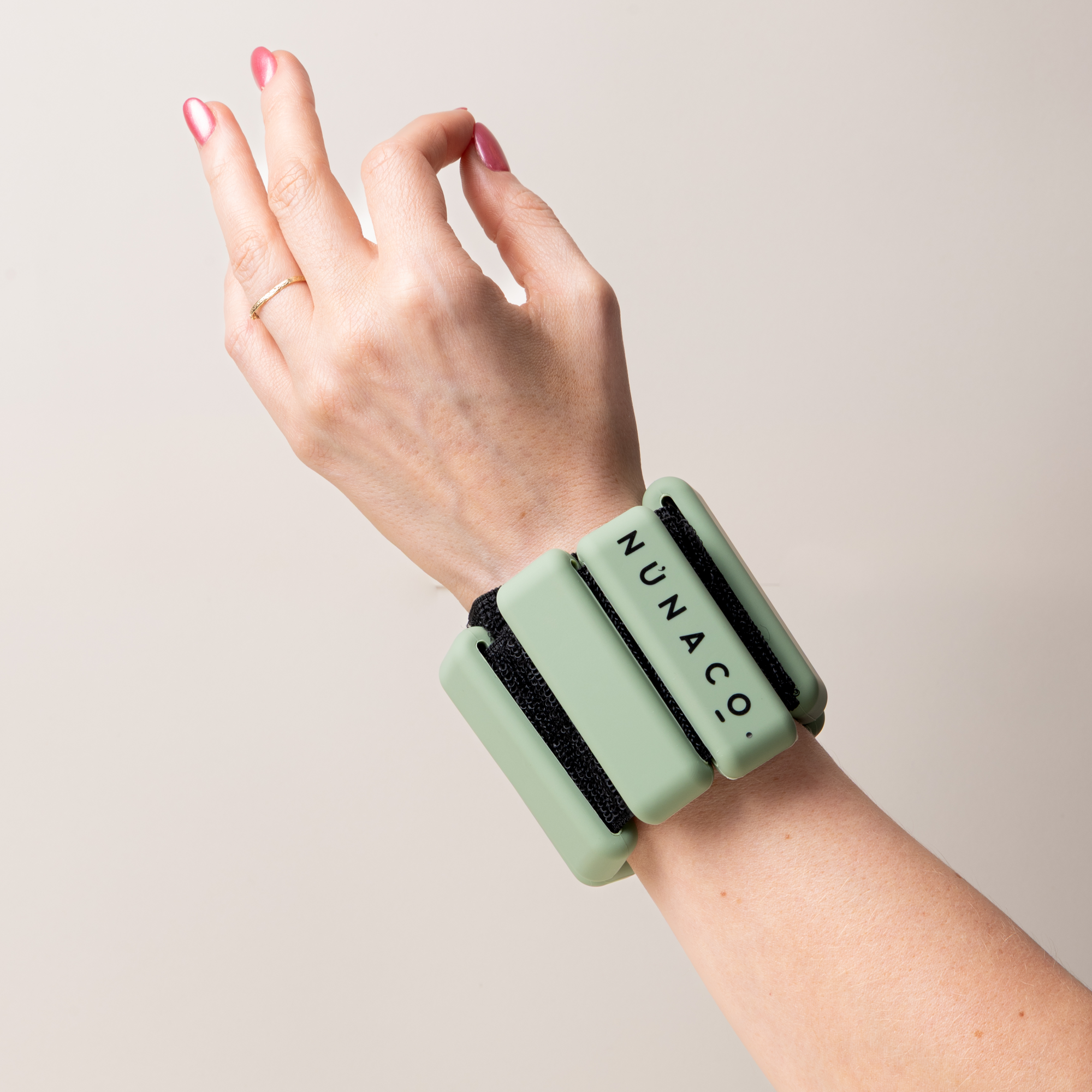 A person's hand and wrist wearing a mint green wrist cuff with black elastic bands and the brand name 'NUNACO' printed on it, set against a plain light beige background.